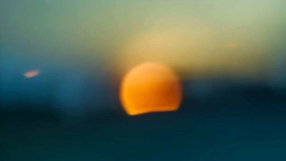 A soft orange sun setting over deep blue water