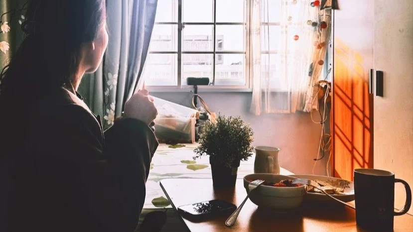 A person at a breakfast table with a cup and bowl, in warm morning light